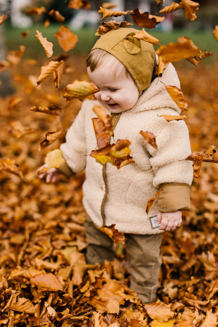 Bambino che gioca con le foglie autunnali di un parco